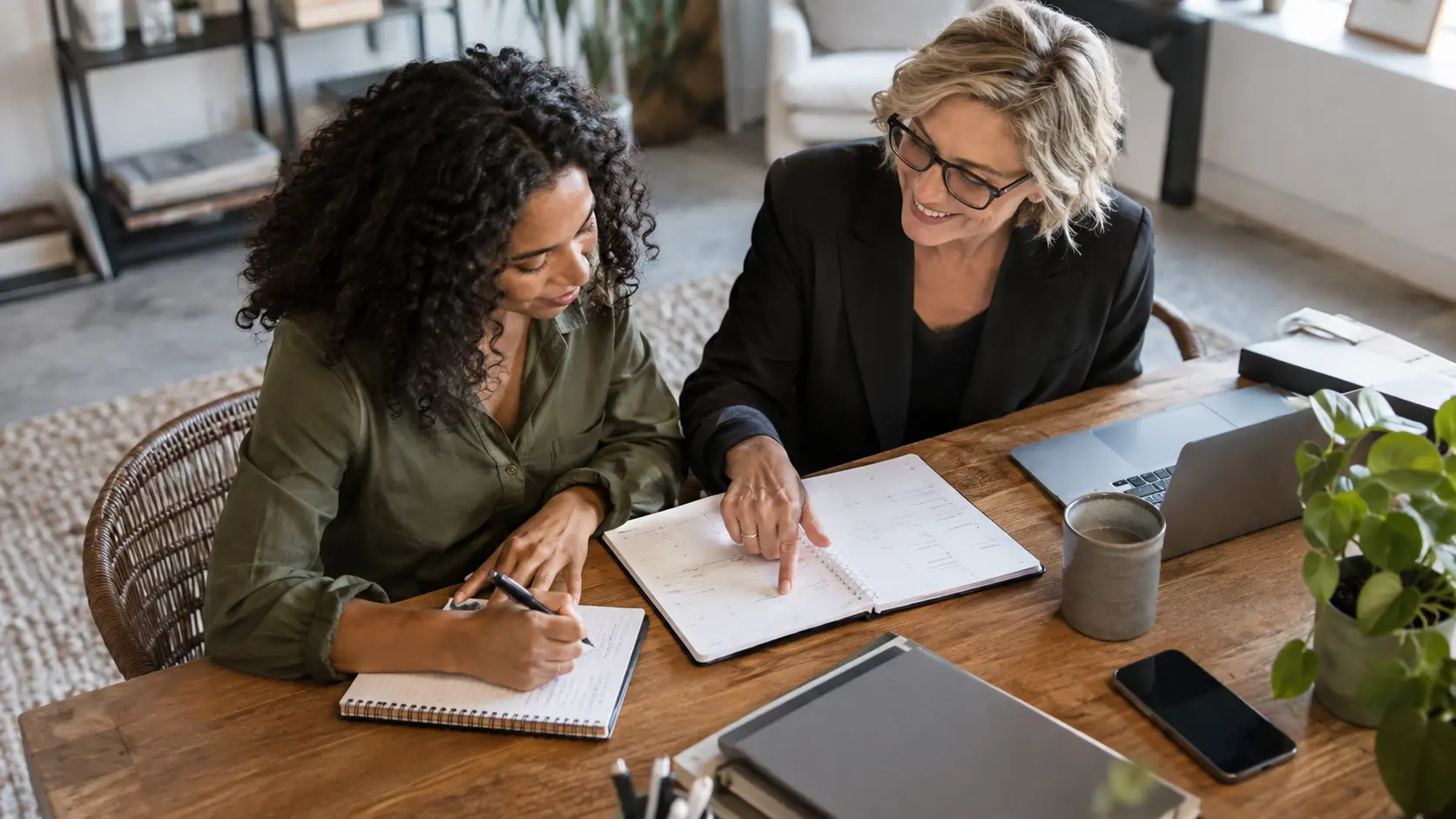 Two women reviewing a notebook and writing an action plan